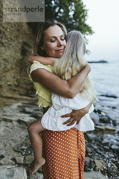 Lächelnde Frau mit Tochter im Arm am Strand