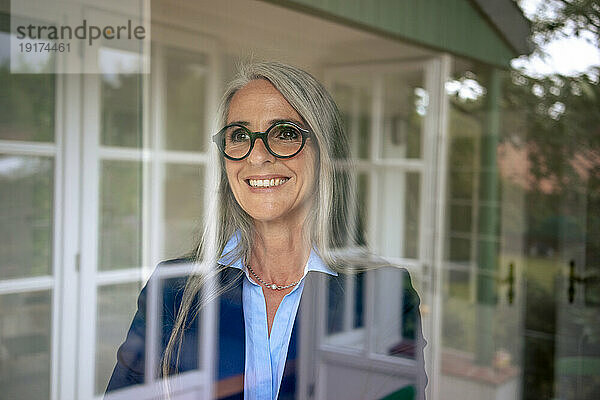 Happy businesswoman with gray hair seen through glass