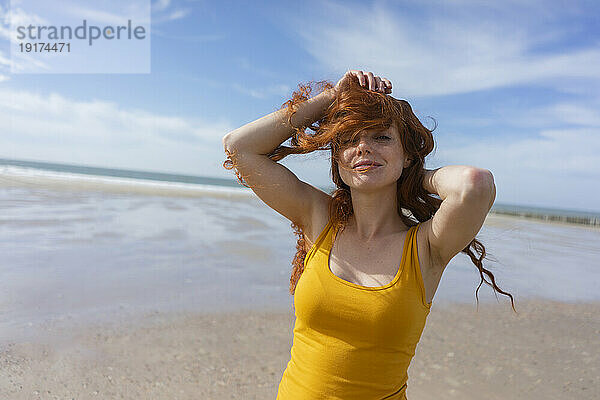 Frau spielt im Urlaub mit zerzausten Haaren am Strand