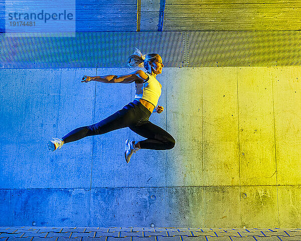 Frau springt vor neonfarbener Wand