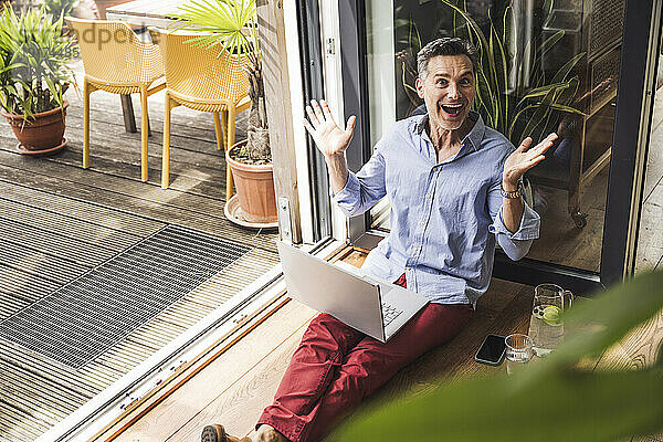 Portrait of happy man using laptop by open balcony