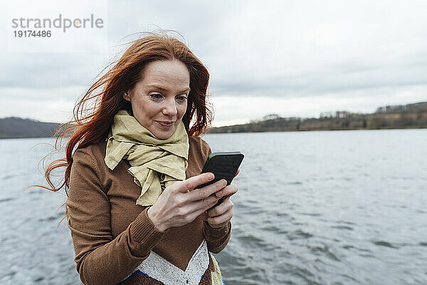 Rothaarige Frau benutzt Mobiltelefon am See
