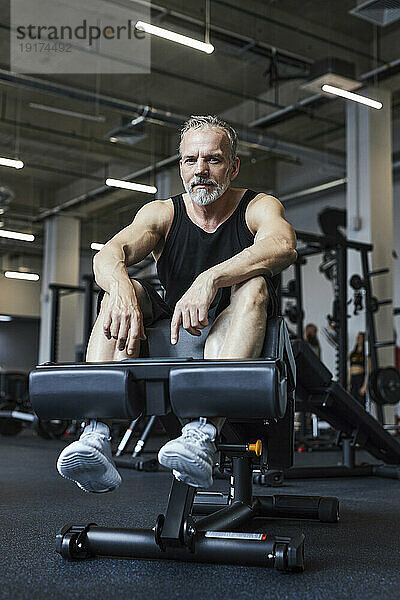Bärtiger reifer Mann entspannt sich auf Trainingsgeräten im Fitnessstudio