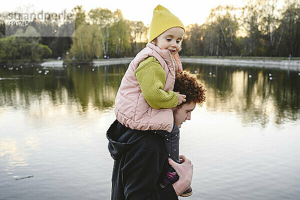 Bruder trägt Schwester auf Schultern am See im Park