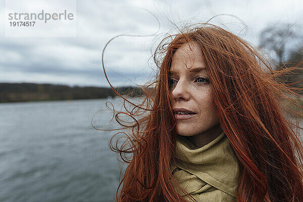 Nachdenkliche rothaarige Frau vor dem See