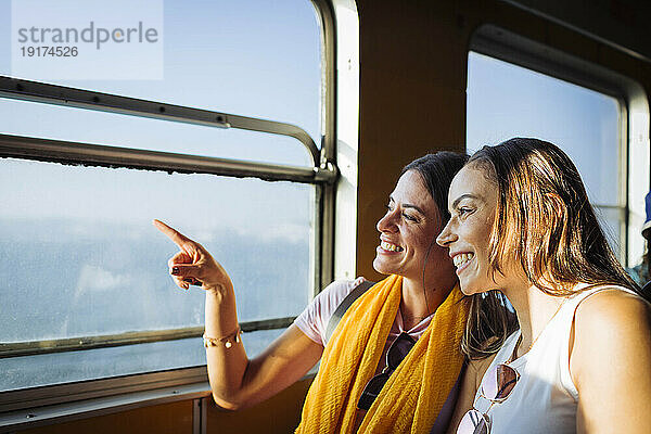 Lächelnde Frau mit Freundin gestikuliert durch Fenster im Zug