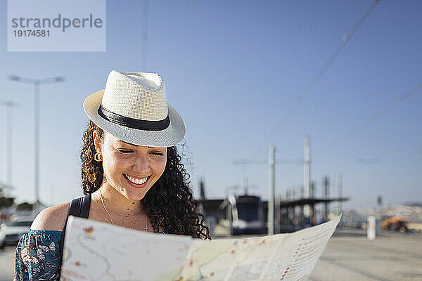 Lächelnde Frau mit Hut blickt an einem sonnigen Tag auf die Karte