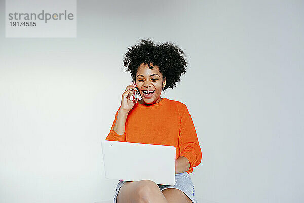 Fröhliche Frau benutzt Laptop und telefoniert vor weißem Hintergrund