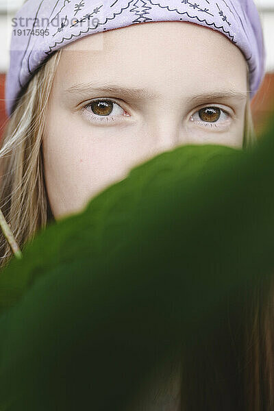 Girl wearing headband hiding face with leaf