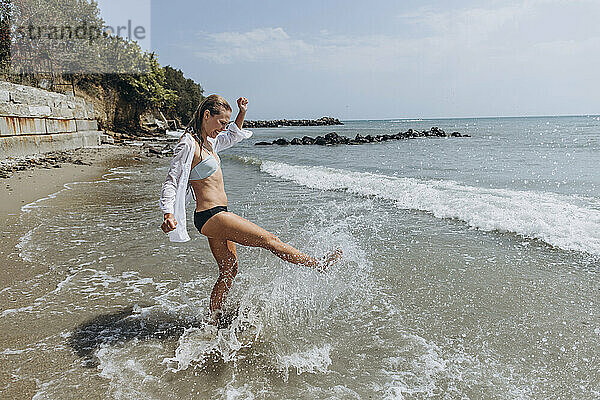 Verspielte Frau spritzt am Strand mit dem Bein Wasser