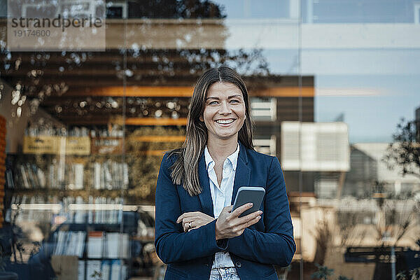 Lächelnde Geschäftsfrau hält Smartphone vor Glas