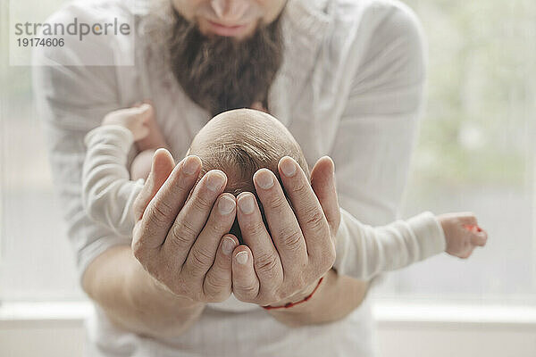 Father with hands cupped carrying newborn daughter