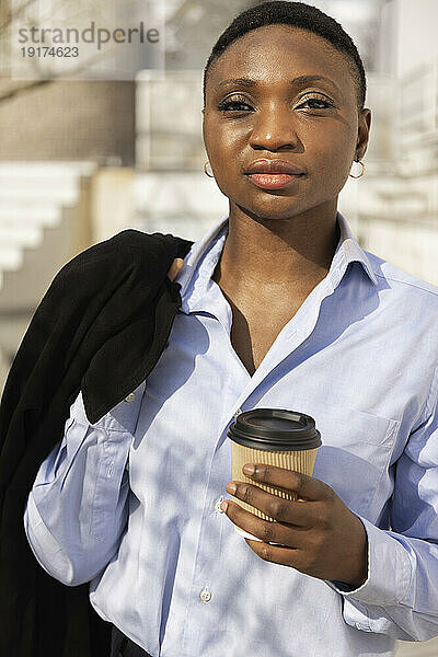 Geschäftsfrau steht an einem sonnigen Tag mit einer Kaffeetasse
