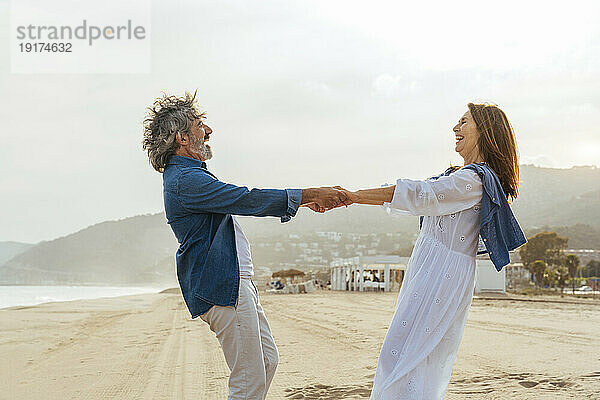Fröhliches älteres Paar hält Händchen und steht zusammen am Strand