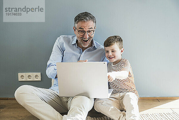 Fröhlicher Großvater und Enkel nutzen Laptop zu Hause