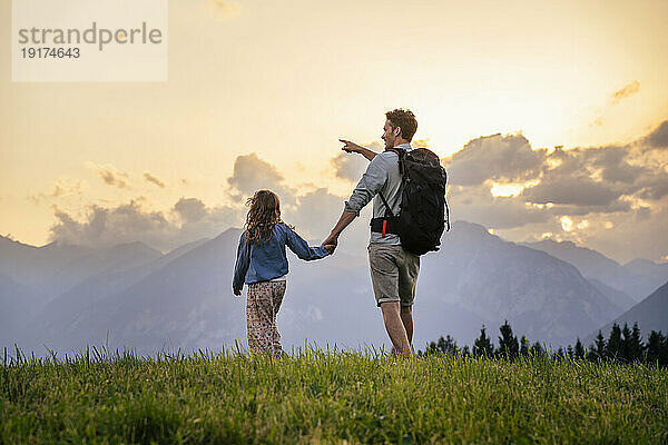 Mann hält die Hand seiner Tochter und geht bei Sonnenuntergang auf der Wiese spazieren