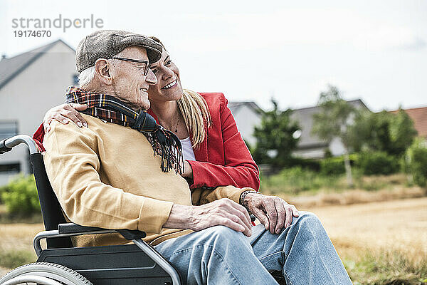 Lächelnde Frau umarmt älteren Mann im Rollstuhl