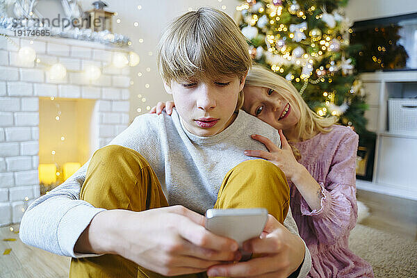 Junge benutzt Smartphone mit Schwester zu Hause an Weihnachten