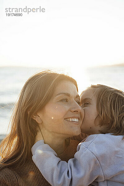 Girl kissing mother at beach on weekend