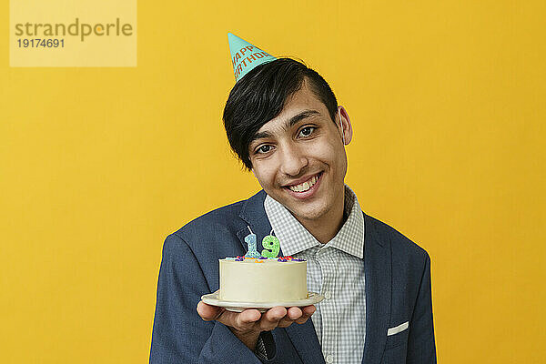 Lächelnder Mann zeigt Geburtstagstorte vor gelbem Hintergrund