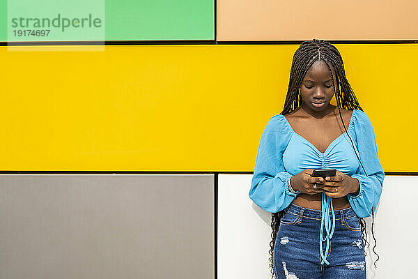 Junge Frau benutzt Smartphone vor bunter Wand