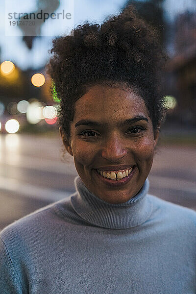 Lächelnde junge Frau auf der Straße in der Abenddämmerung