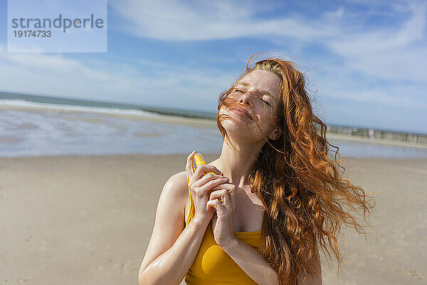 Lächelnde Frau trägt im Sommerurlaub am Strand Sonnencreme auf