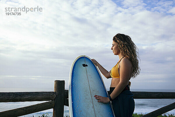 Young woman with surfboard looking at sea