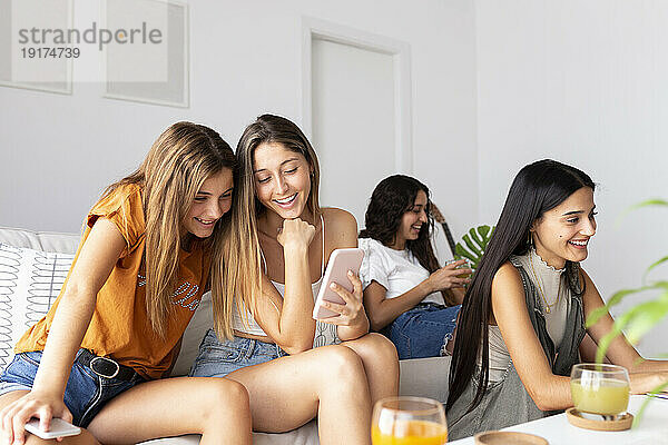Glückliche Freunde  die zu Hause auf dem Sofa sitzen und ihr Smartphone nutzen