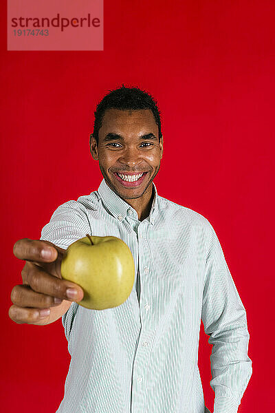 Lächelnder Mann zeigt grünen Apfel vor rotem Hintergrund