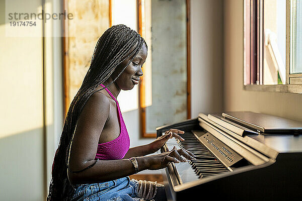 Smiling young woman playing piano at home