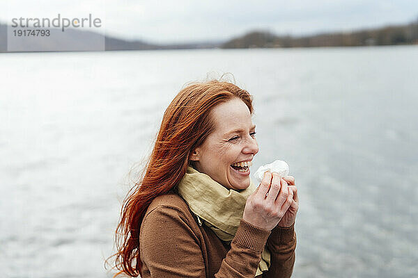 Rothaarige Frau hält Seidenpapier in der Hand und lacht am See