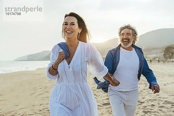 Glückliche Frau hält Händchen mit Mann  der am Strand spaziert