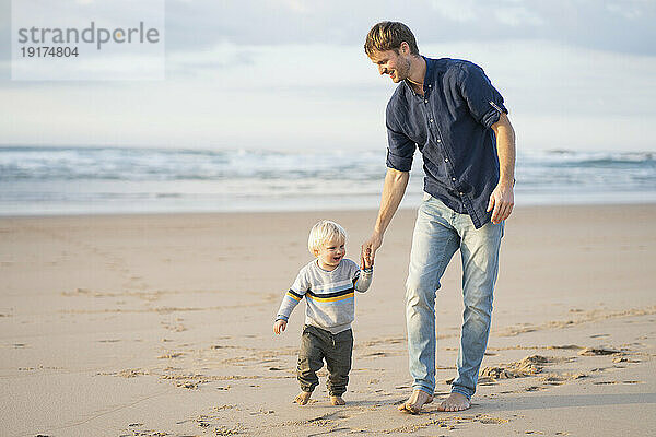 Glücklicher Vater hält Händchen mit seinem Sohn am Strand