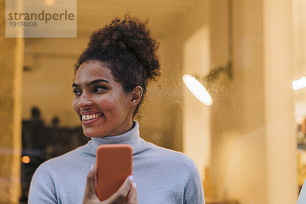 Lächelnde junge Frau mit Smartphone vor Glas