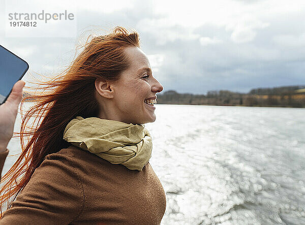 Fröhliche Frau mit Smartphone und Blick auf den See