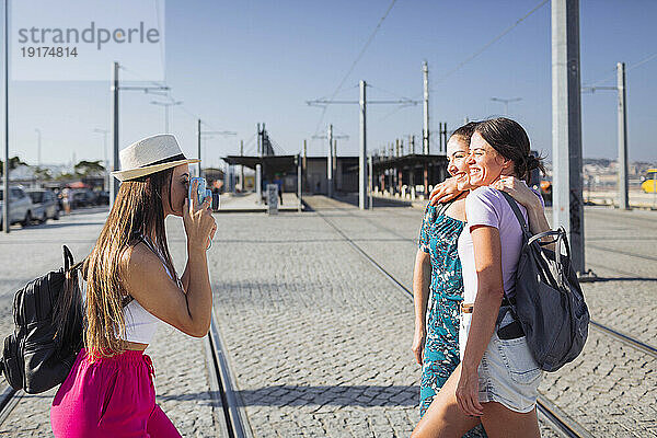 Frau mit Hut fotografiert Freunde mit der Kamera an Straßenbahngleisen an einem sonnigen Tag