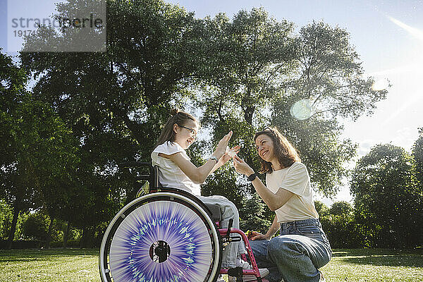 Glückliche Tochter im Rollstuhl mit Mutter im Park an einem sonnigen Tag