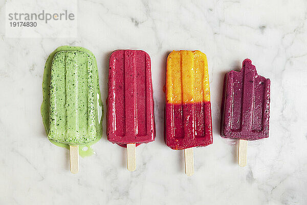 Homemade berry fruit popsicles flat laid against marble background