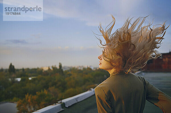 Unbeschwerte blonde Frau genießt den Sonnenuntergang auf dem Dach