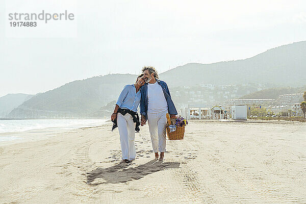 Glückliche Frau umarmt Mann und geht mit Korb am Strand spazieren