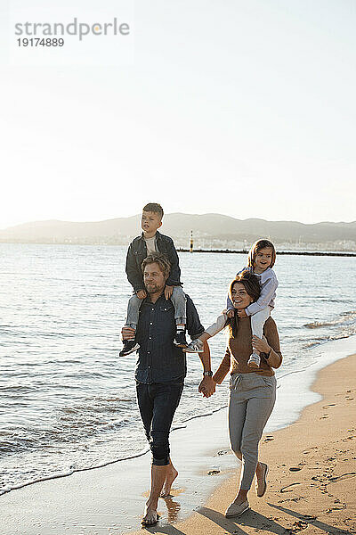 Eltern tragen ihre Kinder auf den Schultern und gehen an einem sonnigen Tag auf dem Seeweg spazieren