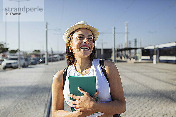 Glückliche Frau mit Hut und Buch an einem sonnigen Tag