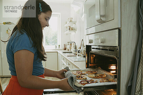 Lächelndes Mädchen  das zu Hause Pizza im Ofen backt