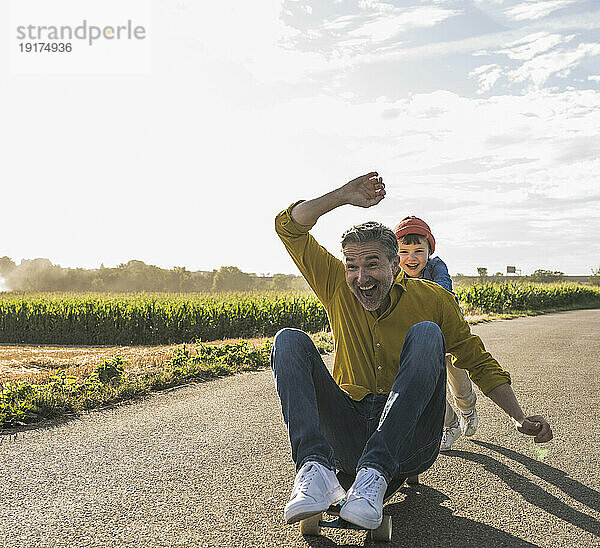 Fröhlicher Enkel schiebt Großvater auf Skateboard auf der Straße