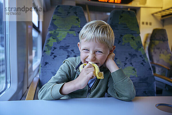 Fröhlicher Junge  der im Zug Banane isst