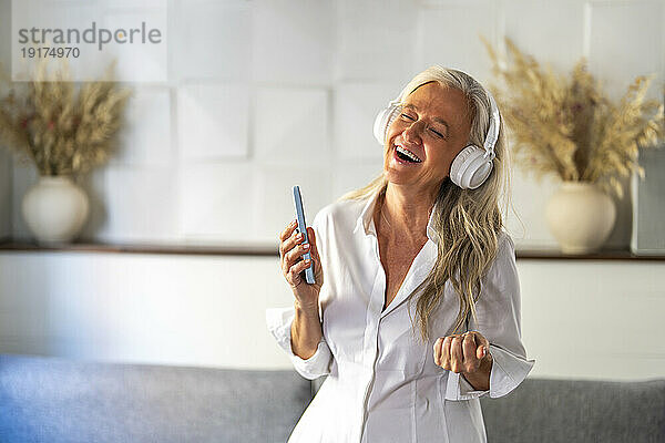 Happy woman wearing wireless headphones listening to music at home