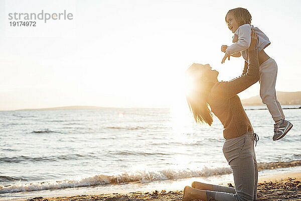 Glückliche Mutter hebt ihre Tochter am Strand in die Luft