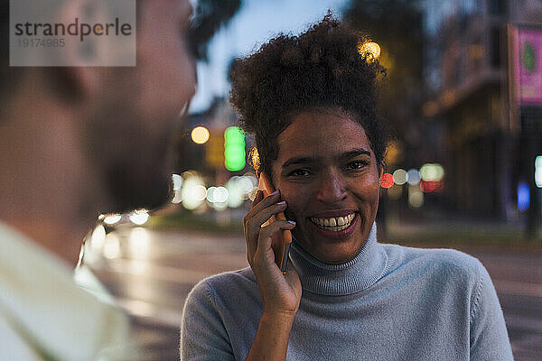 Lächelnde junge Frau  die auf dem Smartphone spricht