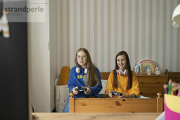 Lächelndes Mädchen spielt Videospiel mit Freund im Schlafzimmer